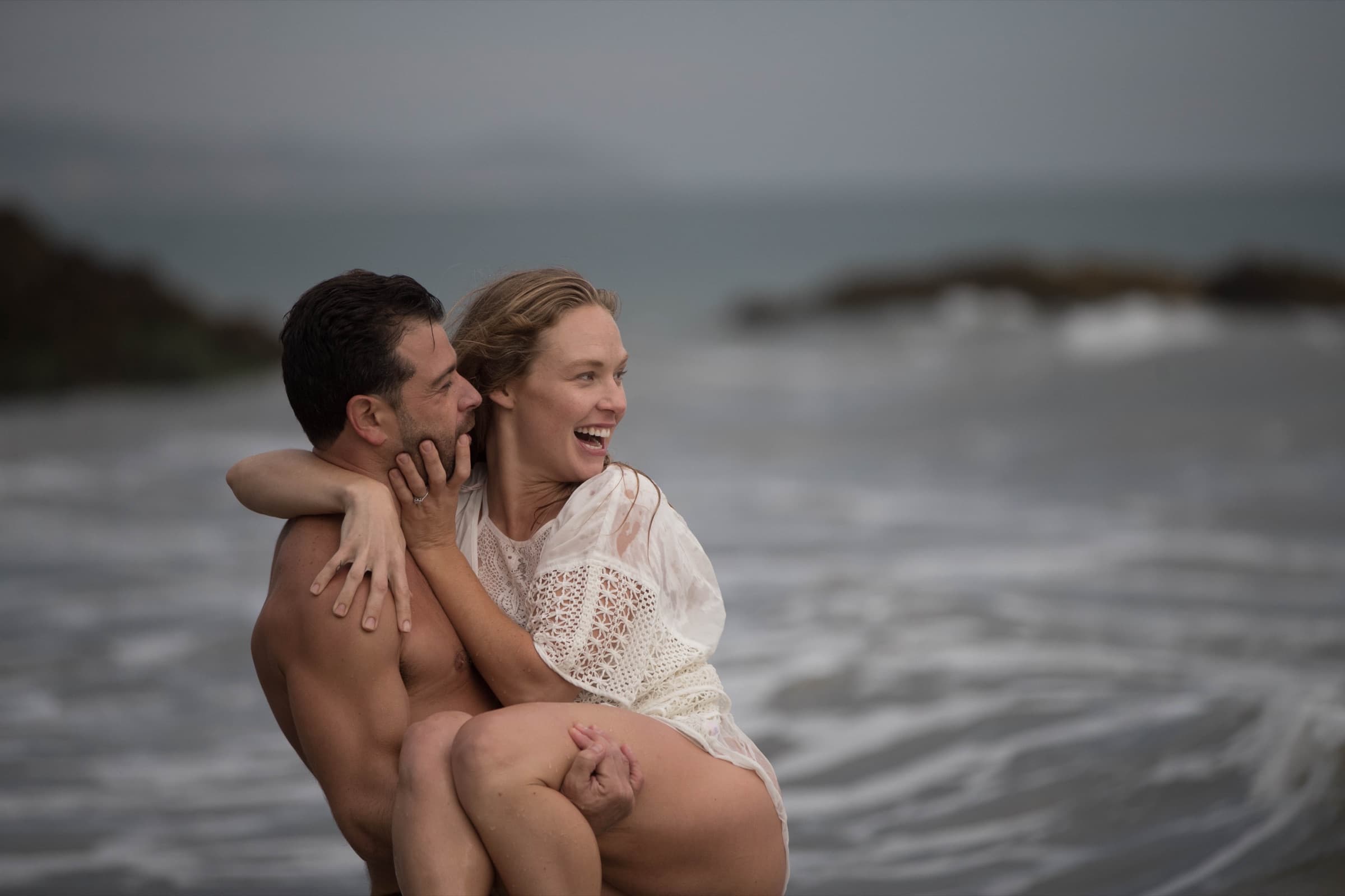 A couple laughing together on an overcast shoreline
