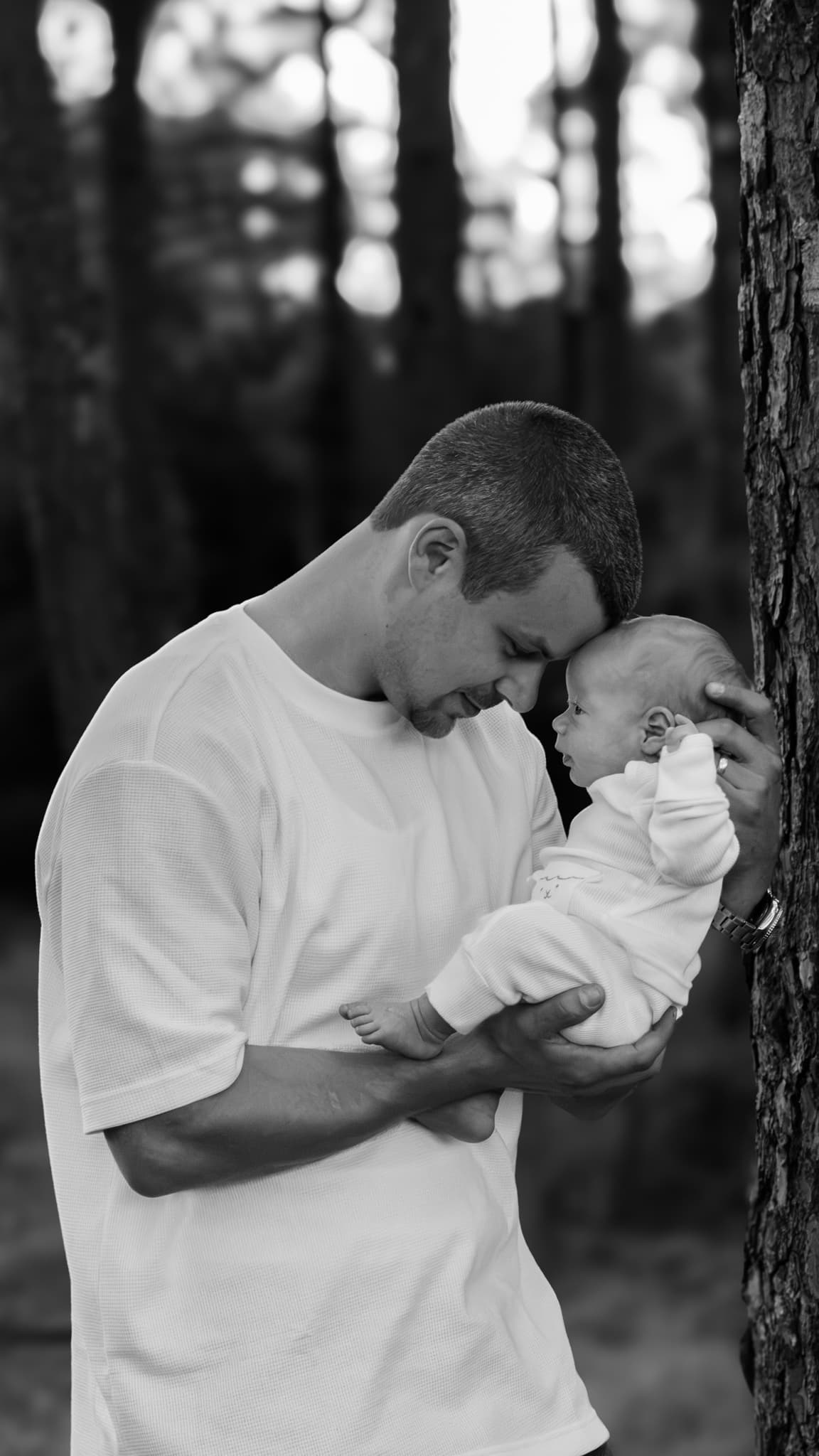 A father cradles his newborn beside a tree