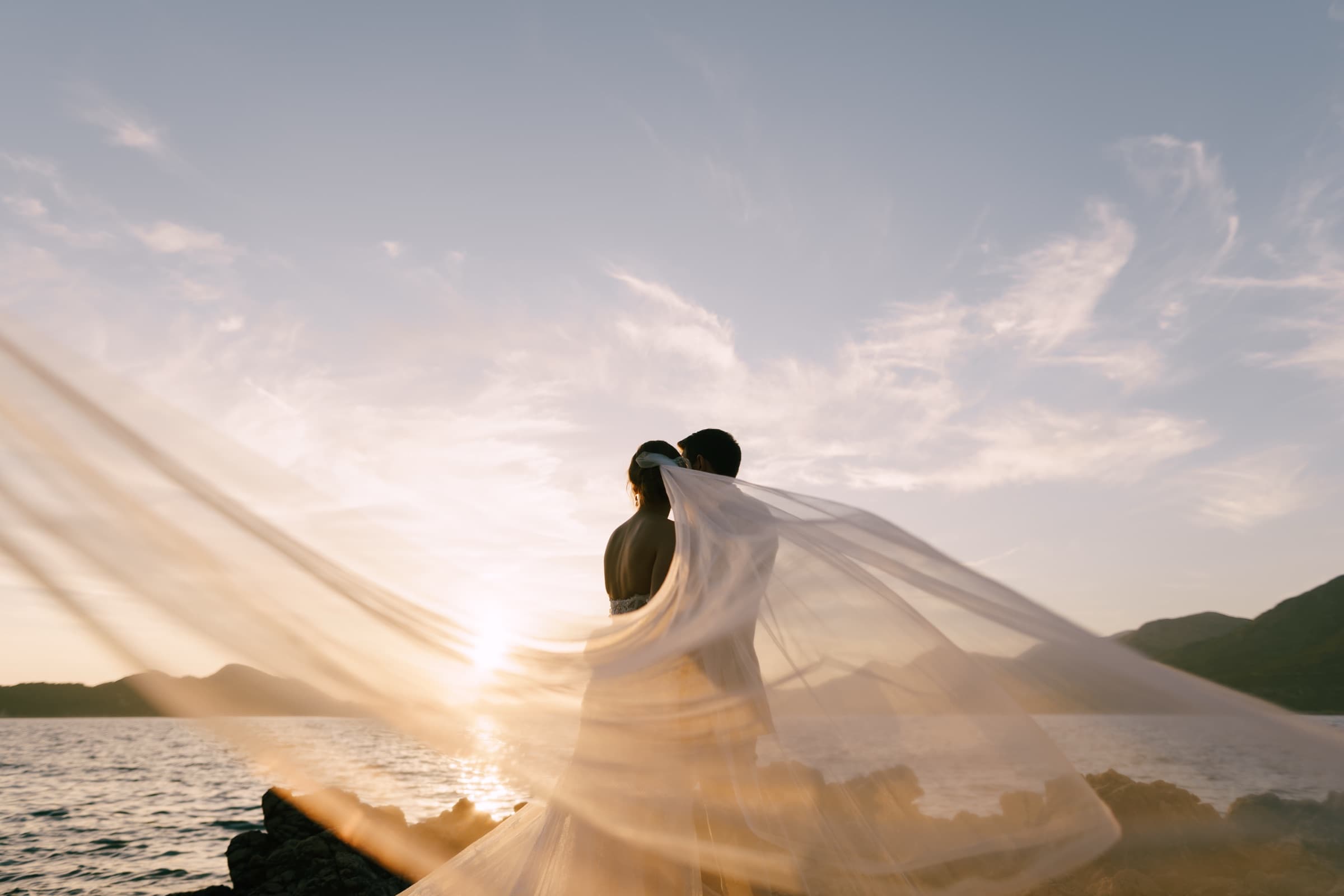 A bride and groom at sunset, her veil catching the wind